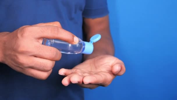 Młody człowiek ręka za pomocą żel dezynfekujący na niebieskim tle — Wideo stockowe