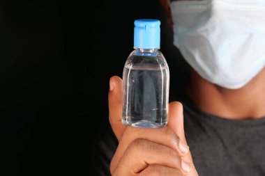 Yüz maskeli bir adam dezenfektan jel tutuyor. 