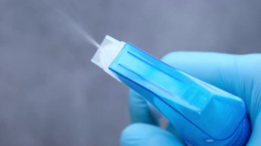 Elinde sprey şişesi olan ve düz yüzeyi silen mavi lastik eldivenler. 