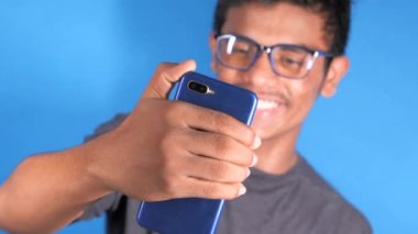 Gözlüklü, gülümseyen genç adam bir video görüşmesi yapmak için telefonunu kullanıyor.