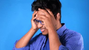 Sıradan giysili üzgün genç adam, yüzünü eliyle kapatıyor..