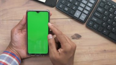 Ofis masasında akıllı telefon kullanan bir adamın üst görüntüsü. 