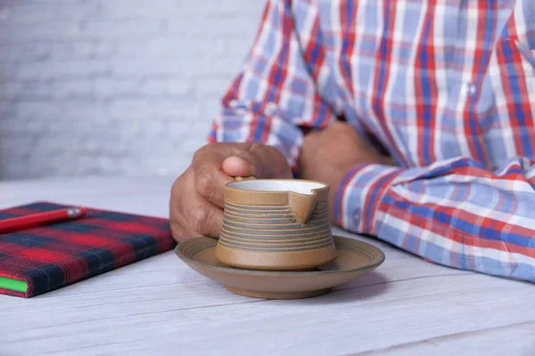 Mladý muž pije čaj s poznámkovým blokem a tužkou na stole — Stock fotografie