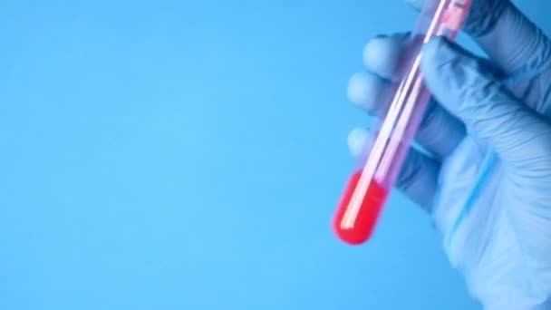 Técnico de laboratorio mano sosteniendo tubo de análisis de sangre sobre fondo azul — Vídeo de stock