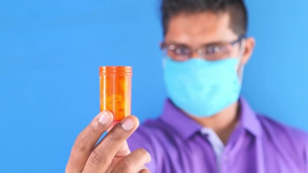 Молодой человек в маске держит контейнер с таблетками — стоковое видео