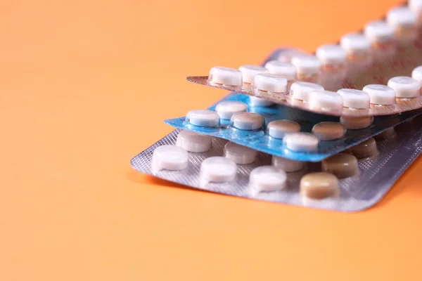 birth control pills on orange background, close up