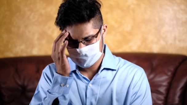 Ein kranker Mann mit Schutzmaske im Gesicht sitzt auf dem Sofa — Stockvideo