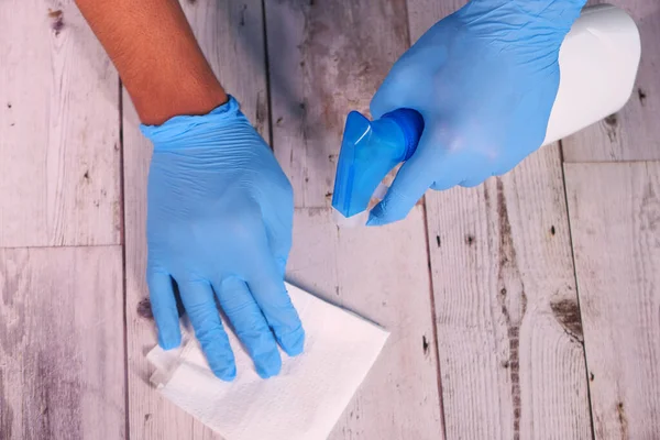 Mano en guantes de goma azul sosteniendo la botella de aerosol y limpiando la superficie plana —  Fotos de Stock
