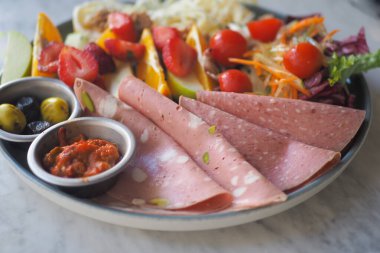 Canlı bir tabakta çeşitli meyveler ve sosisli sandviçler var..