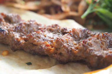 Yanında otlar ve salata olan bir ekmeğin üzerine ızgara et şişleri..