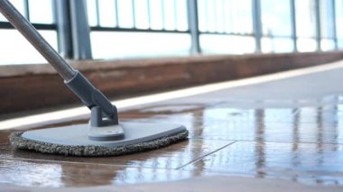 Birisi yüksek katlı bir balkonun ahşap zeminini paspasla temizliyor..