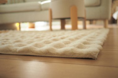 Lüks beyaz bir halı, koltuğun yanındaki açık ahşap zeminde yatıyor..