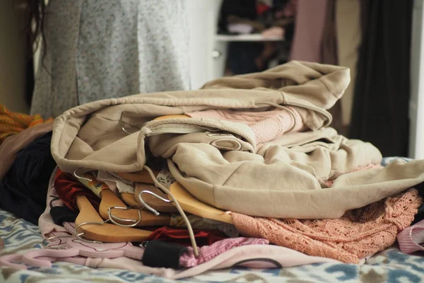 Askılar ve kumaşlarla çevrili çeşitli giysiler bir yatağın üzerinde duruyor..
