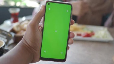 Restoran ortamında elinde yeşil ekranlı akıllı telefon tutan biri..