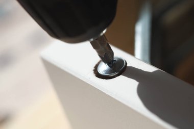 Parlak ışıkta vidayı tahtaya takmak için elektrikli bir alet kullanıyor..