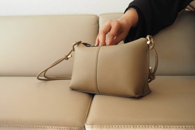 Bir el bej bir kanepede dinlenen şık bir el çantası kapmak üzere..