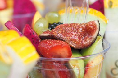 Güneşli bir açık hava etkinliğinde berrak bir fincanda sunulan çeşitli meyveler..