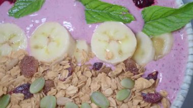 Taze muz, granola ve naneli renkli bir meyve suyu kasesinin tadını çıkarın..