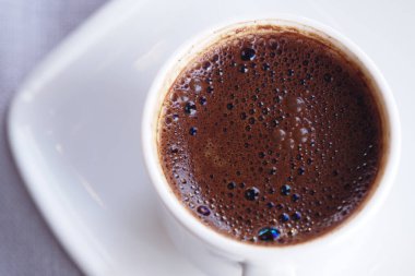 Dumanı tüten bir kahve fincanı beyaz bir çay tabağının üzerinde duruyor, sıcaklığı davet ediyor..