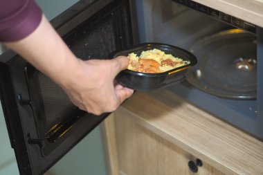 Birisi mikrodalga fırına bir paket yemek koyuyor..