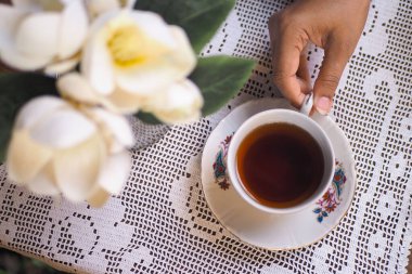 Çiçekler ayarı güzelleştirirken bir insan elinde çay fincanı tutar..