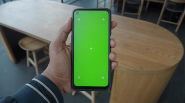 Modern bir kafede yeşil ekranlı akıllı telefon bulunduran kişi.
