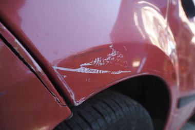 Direksiyona yakın kırmızı bir arabanın çamurluğu çizilmiş..