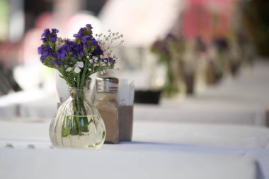 Vazodaki güzel çiçekler dışarıda bir kafede yemek masasını süslüyor.