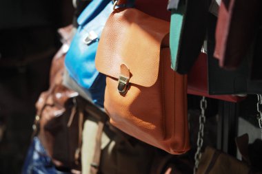 Parlak renkli deri çantalar güneşli bir pazarda bir tezgahta asılı..