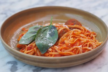 Yemek masasında taze fesleğen ve peynirle kaplı bir tabak makarna..