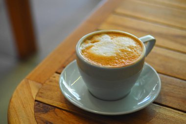 Köpüklü bir fincan kahve ahşap bir masada oturur, sıcaklığı ve rahatlığı davet eder..
