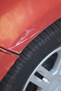 Lastik yakınındaki kırmızı bir arabanın boya hasarına yakın çekim görüntüsü..