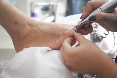 Bir müşteri güzellik salonunda hassas aletlerle pedikür yaptırır..