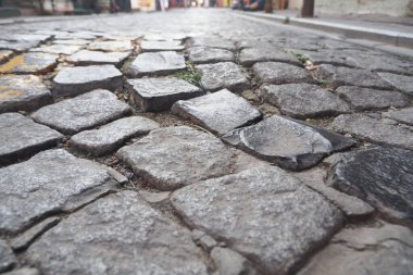 Eski kaldırım taşı sokağında yıpranmış taşlar ve yakınlardaki dükkanlar var..