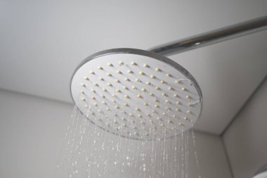 Bir krom duş başlığı çağdaş bir banyo ortamında su püskürtür..