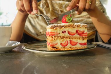 Bir insan masada bir dilim çilekli kekin ve kahvenin tadını çıkarır..