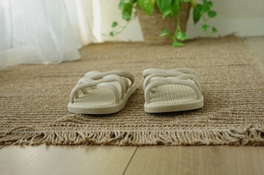 Açık renkli sandaletler güneşli bir odada dokulu bir halının üzerinde dinleniyor..