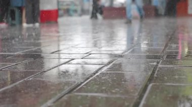 Yağmur yağarken insanlar ıslak sokaklarda yürür, dingin bir hava yaratır..