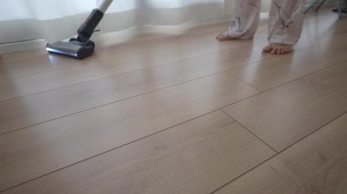 Bir insan güneşli bir yaşam alanında ahşap döşemeleri süpürür..