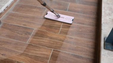 Bir insan ahşap zemini paspasla temizler, parlaklık ve hijyen sağlar..