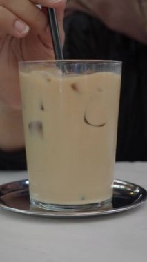 Birisi kafede otururken buzlu kahveyi bardakla karıştırıyor..