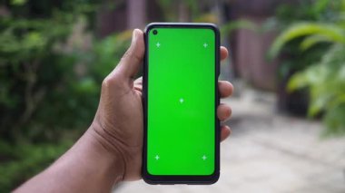 Bahçe ortamında yeşil ekranlı bir akıllı telefon sergiliyor.