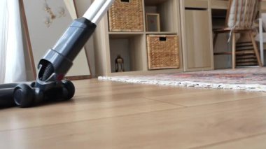 Elektrikli süpürge ahşap zeminde hareket ederek toz ve enkazı topluyor..