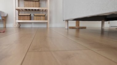 Bir insan oturma odasındaki mobilyaların altını temizlemek için süpürge kullanır..