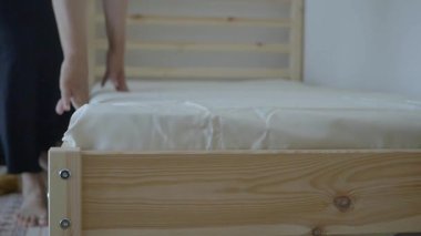 Bir kişi yeni bir yatak çerçevesi ve yatak hazırlar ve monte eder..