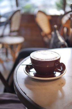 Bir kafedeki küçük bir masada koyu bir kahve fincanı bir tabakta oturur..