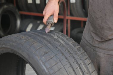 Bir işçi oto tamirhanesinde lastik tamir etmek için bir araç kullanır..