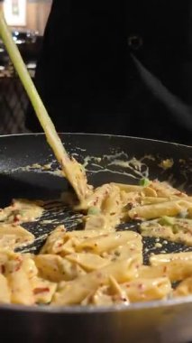 Şef sıcak tavada taze malzemelerle kremalı makarna karıştırır..