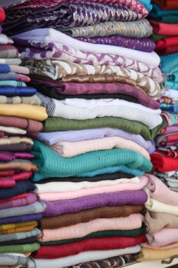 Parlak ve çeşitli kumaşlar düzgün bir pazar ortamında istiflenmiş..