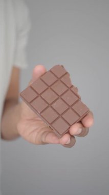 Bir insan ısırık büyüklüğünde bir parça çikolatayı elinde tutar, tadını çıkarmaya hazırdır..